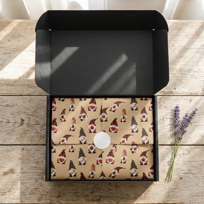 Open black SP Boutique gift box with kraft Christmas tissue paper printed with gnomes in red plaid hats, folded and sealed with a round white sticker